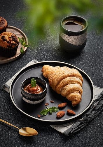 A breakfast plate with coffee and croissant.