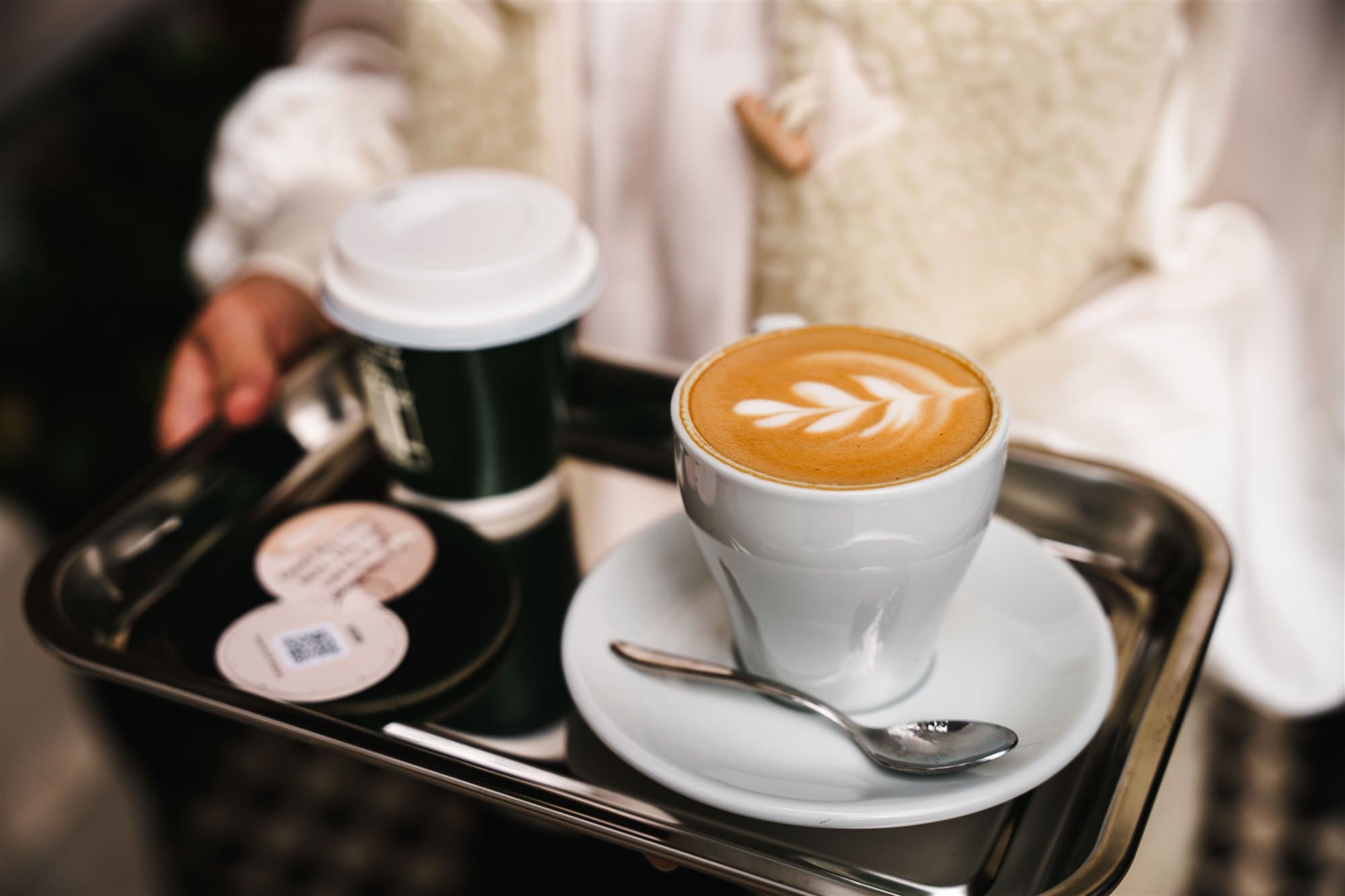 Barista carrying a latte and message cards on a tray.