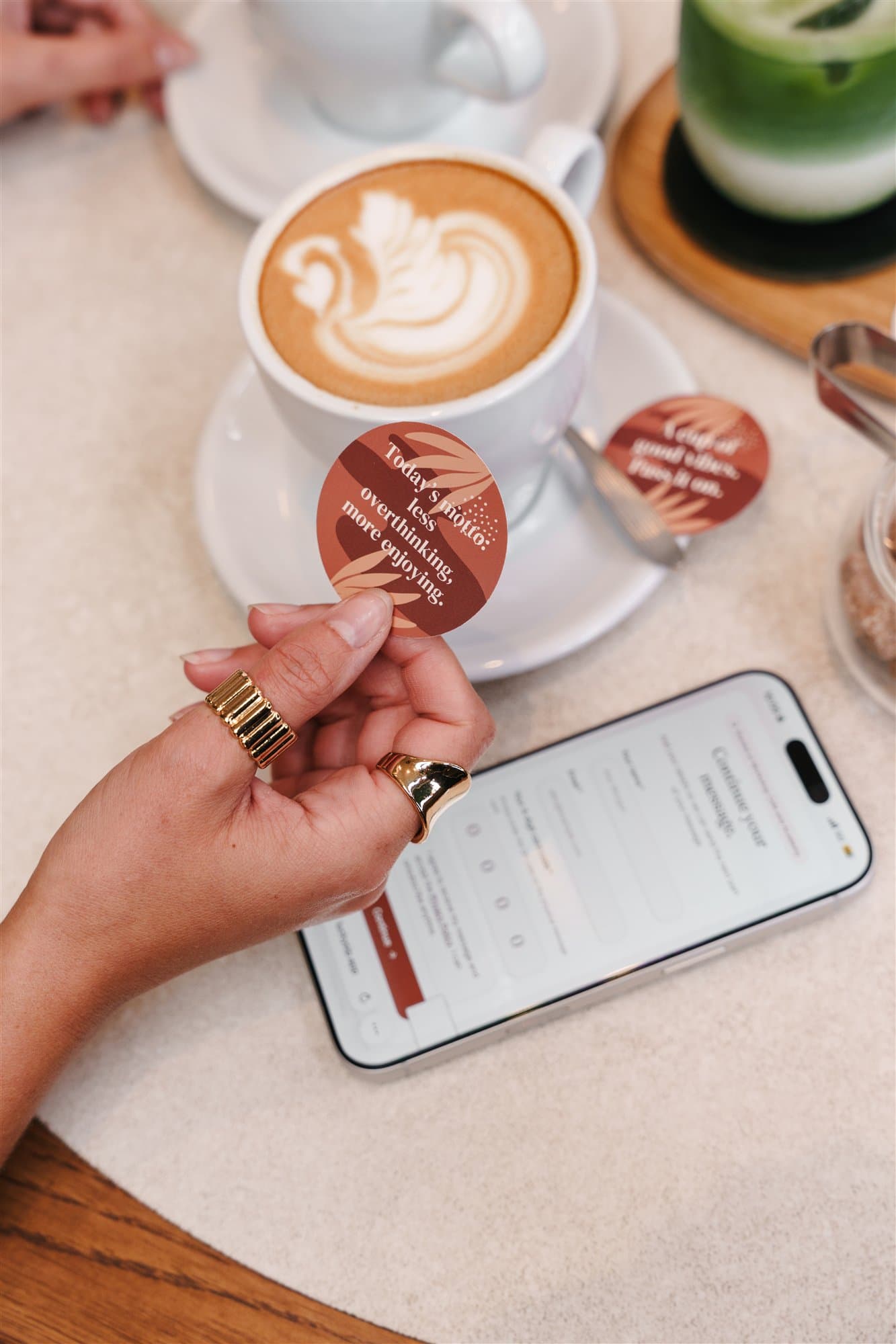Coffee, matcha, pastries, phone and a message card on a café table.