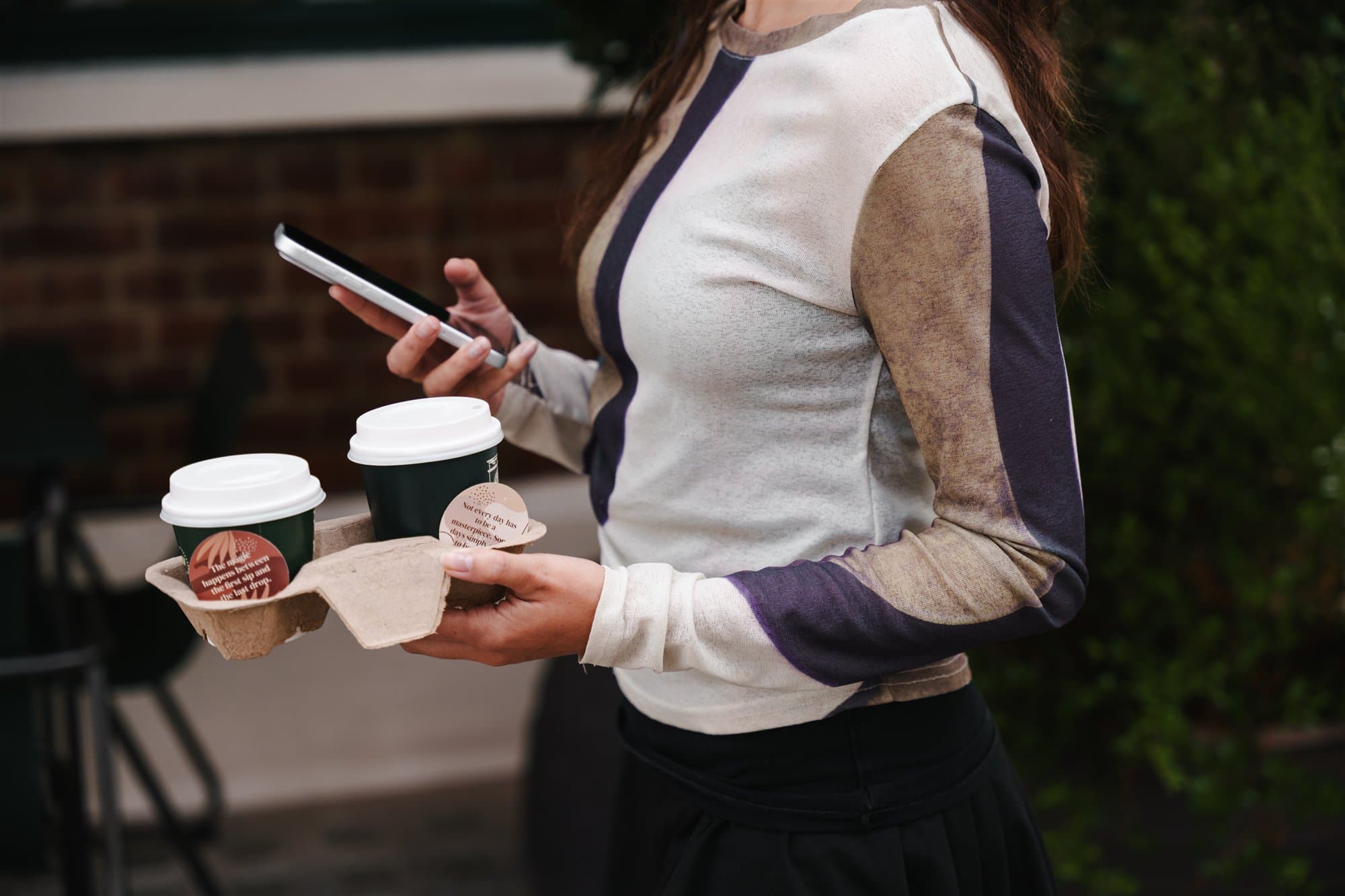 Person carrying two takeaway coffees with message cards.